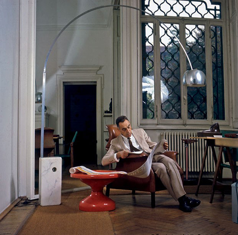 Achille Castiglioni ien su estudio bajo su lámpara arco "Arco" (1962), sentado en su silla"Sanluca" al lado de su mesa"Rochcetto".